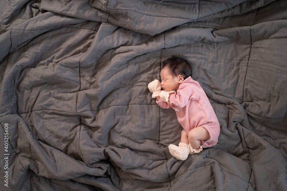 Obraz premium asian baby infant wearing gloves and socks sleeping on gray bed. studio shot.