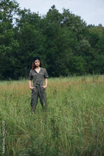 Woman on nature holds his hands in the pockets of green overalls in the meadow 