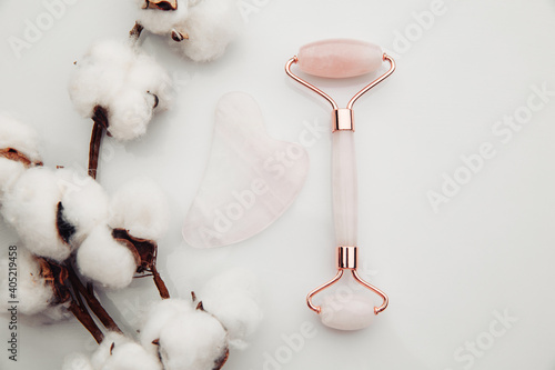 Crystal rose quartz facial roller and massage tool jade Gua sha on a white table. Facial anti-age massage for natural lifting and toning treatment at home.