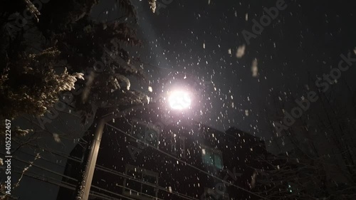 Evening snow falling down a bright streetlight
