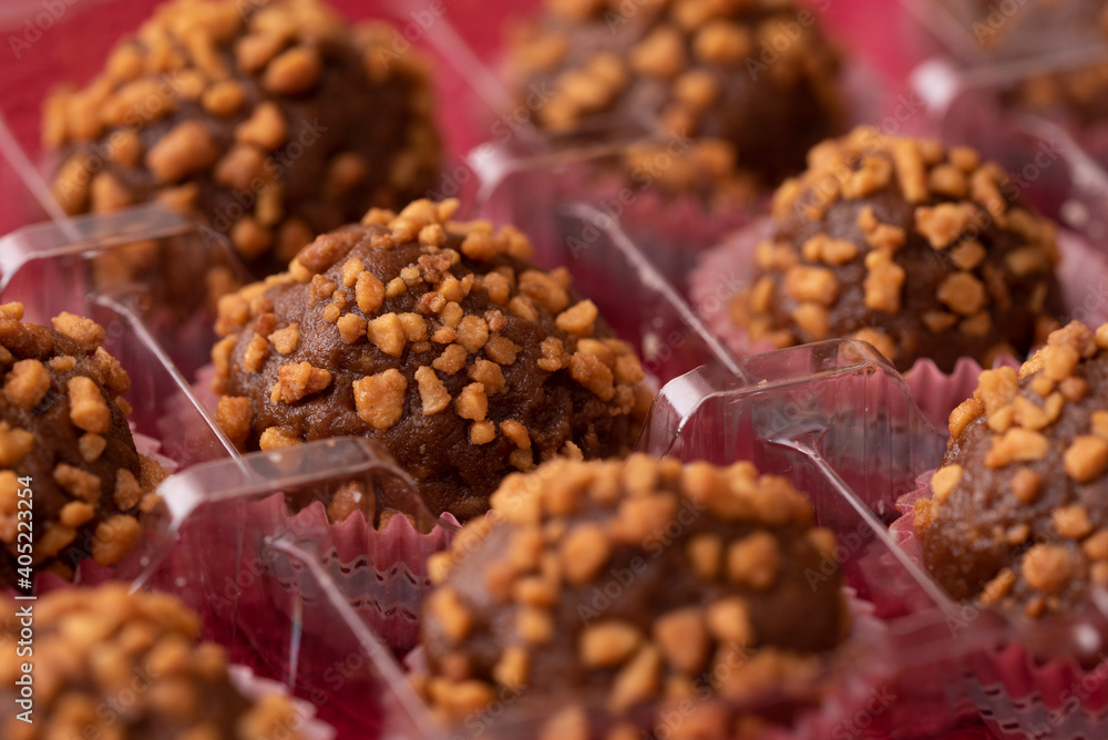 balls of chocolate with peanut praline in a rectangle transparent box on red background, close up view balls of chocolate with peanut praline in a rectangle transparent box on red background, close up view