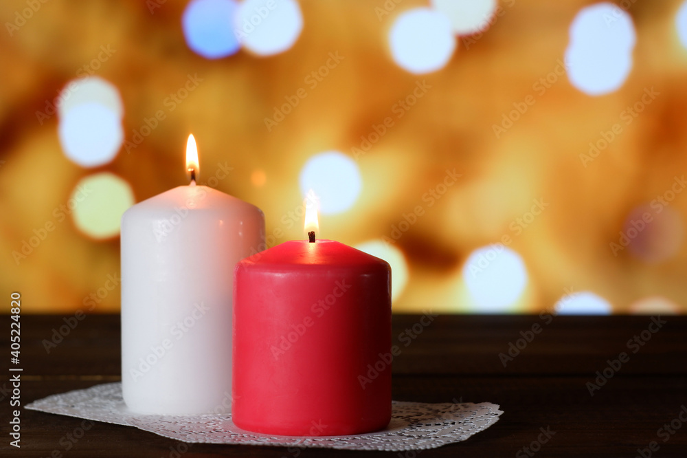 White and pink burning aromatic candles on white openwork paper napkin on wooden table, yellow bokeh lights background closeup view selective focus. Love, Valentine's, women's day, romantic concept White and pink burning aromatic candles on white openwork paper napkin on wooden table, yellow bokeh lights background closeup view selective focus. Love, Valentine's, women's day, romantic concept