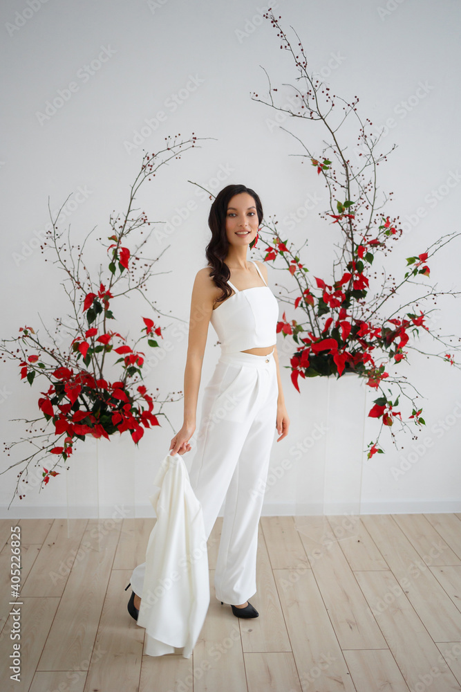 Bride in a white trouser suit posing against the background of an unusual composition of fresh flowers poinsetia for an chamber wedding ceremony