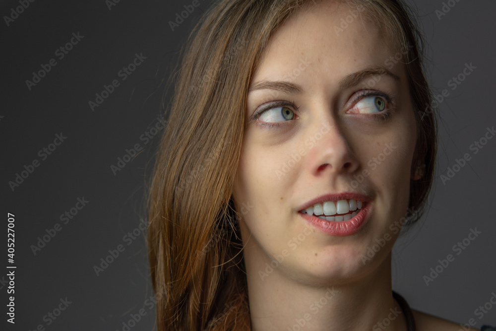 studio close up on the face of young beautiful wondering curious girl with her eyes up to the side. She is on the dark grey background. studio close up on the face of young beautiful wondering curious girl with her eyes up to the side. She is on the dark grey background.