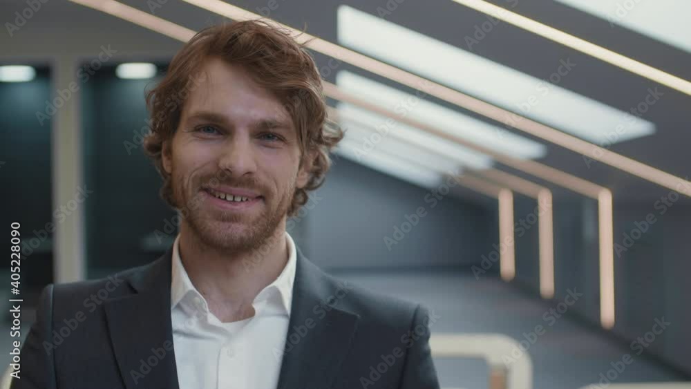 Medium shot portrait of young handsome Caucasian businessman wearing elegant suit sitting in conference hall, looking at camera and smiling Medium shot portrait of young handsome Caucasian businessman wearing elegant suit sitting in conference hall, looking at camera and smiling