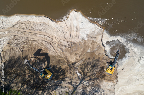Yellow excavator digger working. Excavator digging sand, ground from water. Industrial aerial drone view.