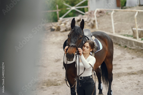 Cute girl with a horse. Lady in a white t-shirt. Woman in a summer ranch.