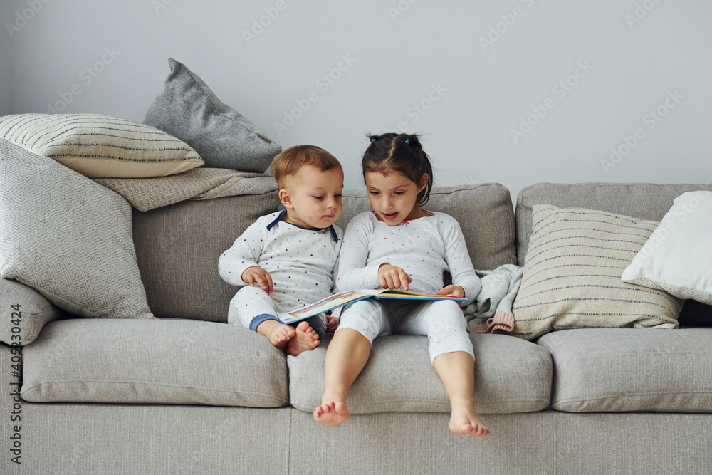 Sister and brother reading book. Interior and design of beautiful modern bedroom at daytime Sister and brother reading book. Interior and design of beautiful modern bedroom at daytime