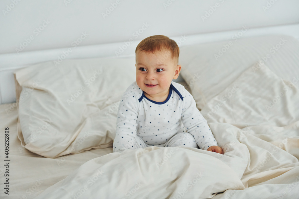 Cute little boy is on the bed. Interior and design of beautiful modern bedroom at daytime