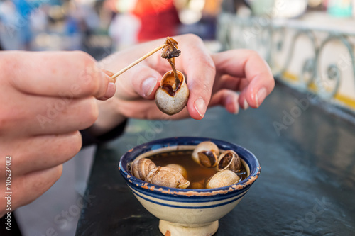 Woman extracting snail from its shell from a soup in Morocco