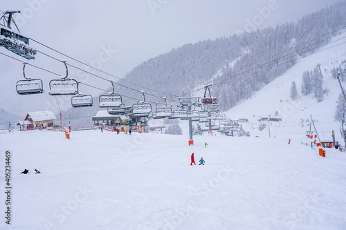 Winter snowing day on a ski resort. Downhill skiing during a heavy snowfall. Ski race for young children. Blurred focus background. High quality photo