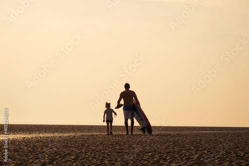 A silhouette of a father and daughter with a paddle board on a beautiful summers day on the calm ocean. Relaxing family bonding time with water sports and exercise. soft and hazy days.