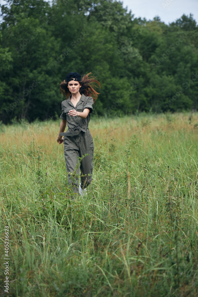 Woman in the meadow running on tall grass in green jumpsuit 