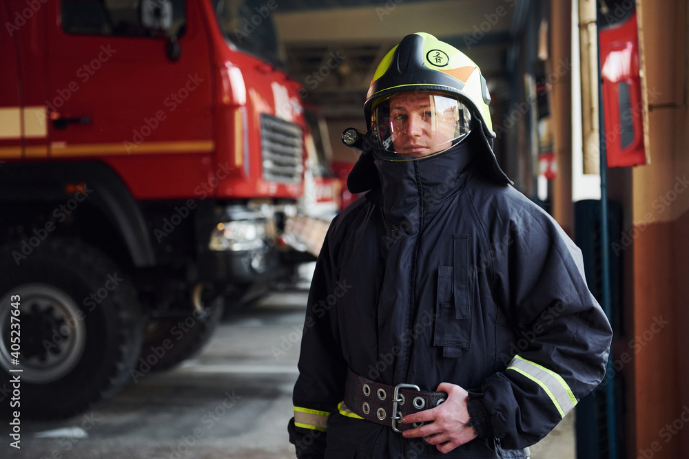 Fototapeta premium Male firefighter in protective uniform standing near truck