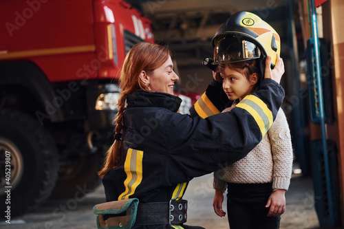 Photographie Happy little girl is with female firefighter in protective uniform