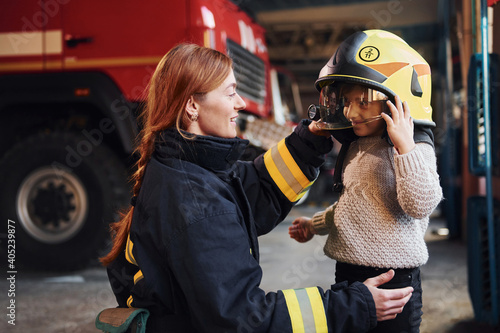Happy little girl is with female firefighter in protective uniform Fototapeta