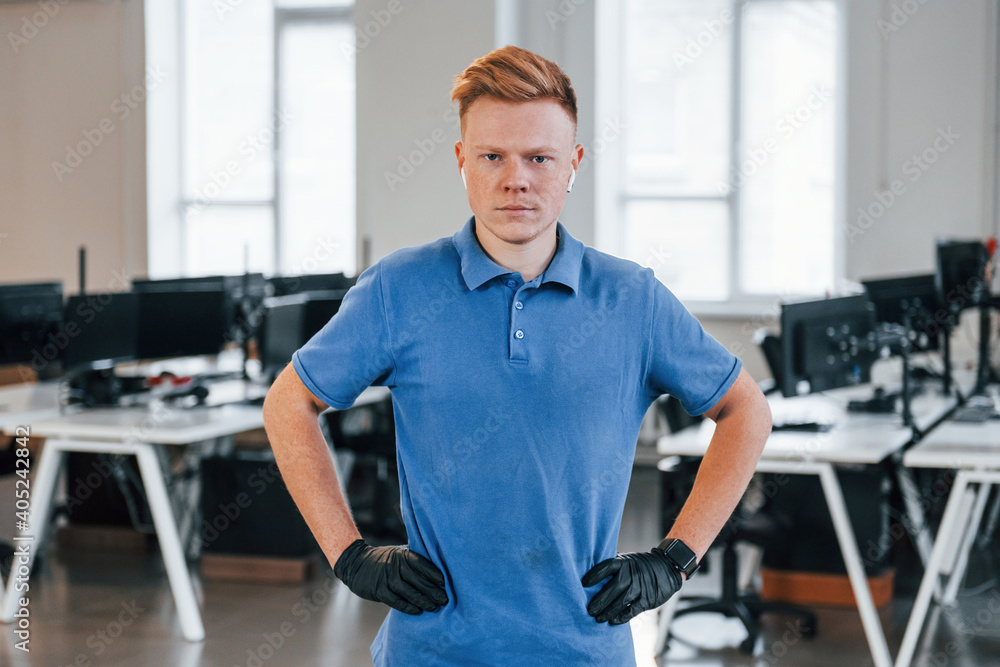 Portrait of young man in blue shirt and black protective gloves. Standing in the office Portrait of young man in blue shirt and black protective gloves. Standing in the office