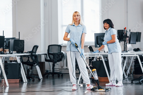 Woman uses vacuum cleaner. Group of workers clean modern office together at daytime