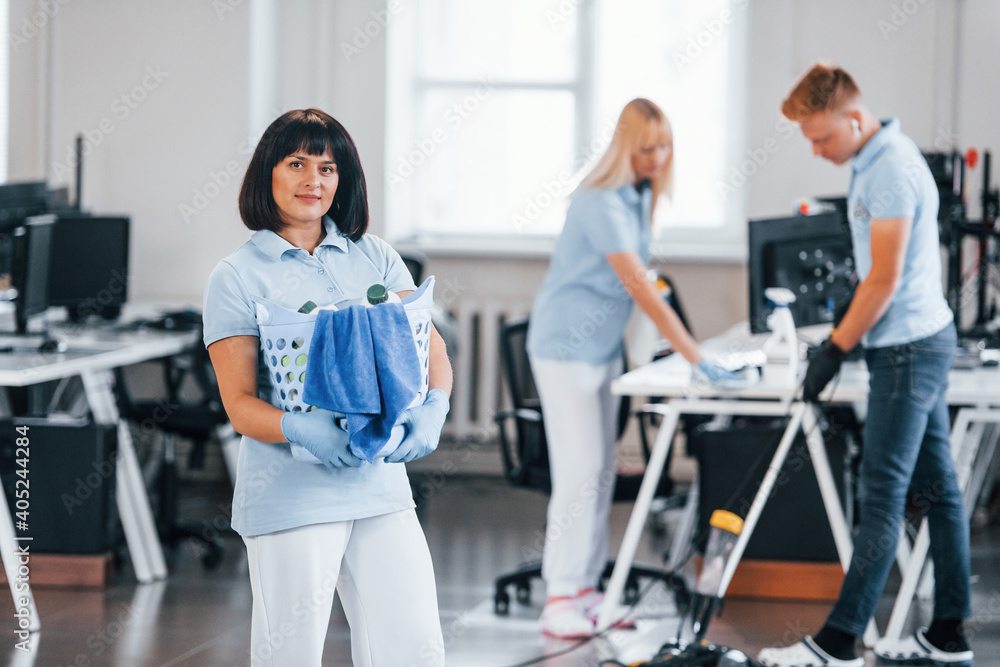 Woman with basket. Group of workers clean modern office together at daytime Woman with basket. Group of workers clean modern office together at daytime