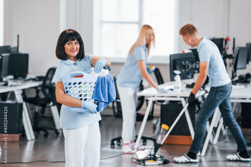 Woman with basket. Group of workers clean modern office together at daytime