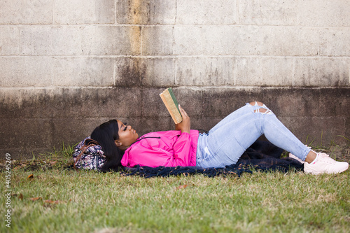 A beautiful African-American teenage girl laying on her back outside reading a book for school for her education © Ursula Page