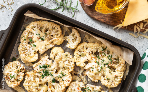 Baked cauliflower with cheese, garlic, herbs, and spices in a baking sheet. Top view. Tasty vegetarian food.