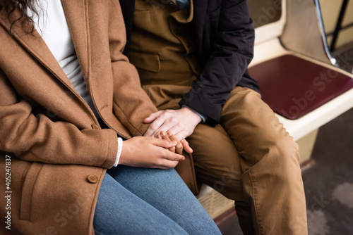 cropped view of interracial couple holding hands while sitting in wagon of subway