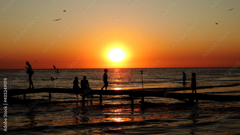 Sunset with silhouettes of people on the pier birds bathing people Sunset with silhouettes of people on the pier birds bathing people