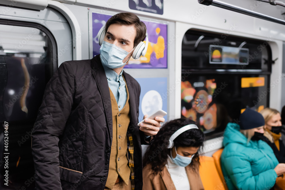 man holding smartphone near african american woman in medical mask on blurred background