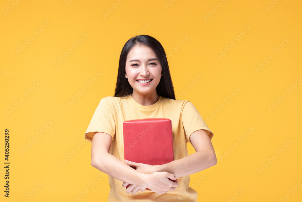 Portrait of happy smiling girl in casual holding gift box and expression face isolated over yellow background Portrait of happy smiling girl in casual holding gift box and expression face isolated over yellow background