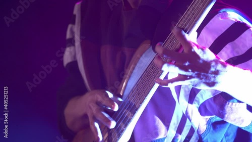 Male guitarist playing electric bass guitar on a rock concert in a club. Red and blue lighting, hands closeup.