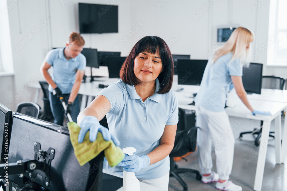 Cleans monitor. Group of workers clean modern office together at daytime Cleans monitor. Group of workers clean modern office together at daytime