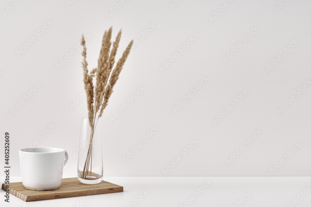 A transparent vase with dry branches and mug on a white background. Minimalism, eco-materials in the interior decor. Copy space, mock up.