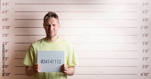 Leinwand Poster arrested prisoner young man holding a placecard in front of the height chart