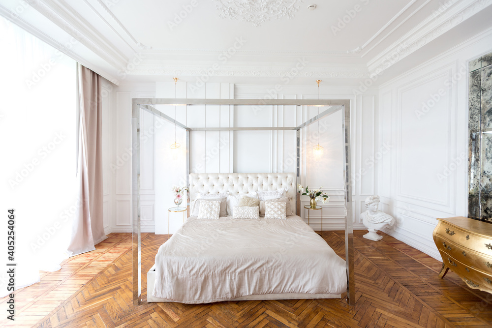 modern interior of a luxurious large bright bedroom. white stucco walls and a large four-poster bed and wooden parquet floor