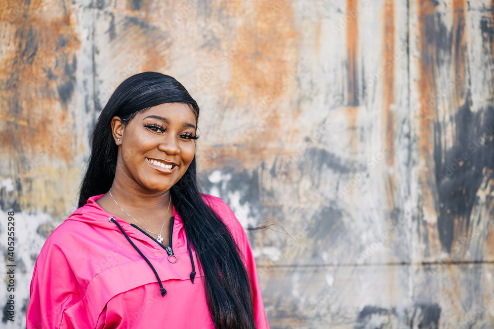 Smiling and happy beautiful African American teenage girl with long hair and a pink magenta jacket standing outside in an urban city setting Smiling and happy beautiful African American teenage girl with long hair and a pink magenta jacket standing outside in an urban city setting