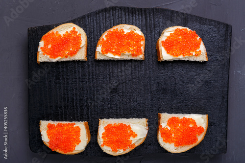 Bruschettes with butter and red caviar laid out on a black board on a gray concrete background copy space.