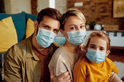 Portrait of smiling parents with daughter wearing face masks at home due to COVID-19 pandemic.