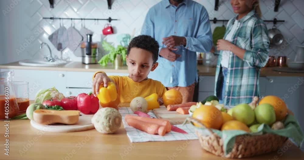 Lovely preteen african boy putting fruit and vegetables on table in the kitchen. Happy couple of parents smiling cheerful on background. Lovely preteen african boy putting fruit and vegetables on table in the kitchen. Happy couple of parents smiling cheerful on background.