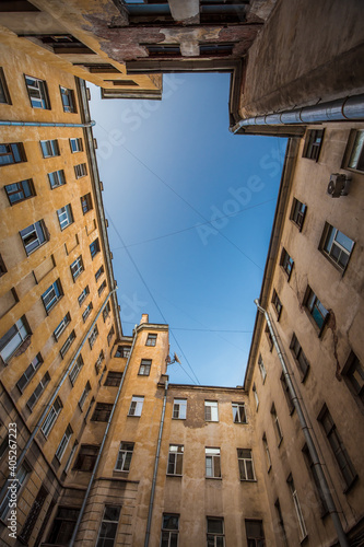 Bottom-up view from a rectangular courtyard surrounded by multi-storey buildings. The blue sky above the courtyard is crossed by intersecting wires. European city. No people