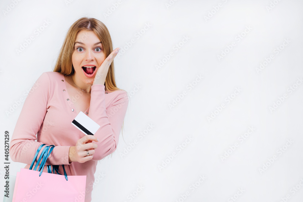 Happy impressed amazed young woman holding credit credit card and packages after shopping on white background Happy impressed amazed young woman holding credit credit card and packages after shopping on white background