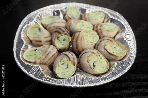 a lot of freshly prepared grape snails with green oil and garlic lie in a silver container on a black background of a side view .food in France snails in Burgundy