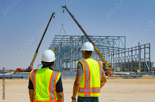 Two industrial construction workers looking at a steel structure on a construction site
