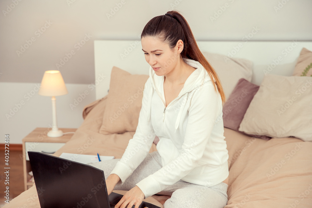 woman working on laptop. Young woman in white is working on the computer in bed. Working in the bedroom. Home office during the pandemic. Working from home. woman working on laptop. Young woman in white is working on the computer in bed. Working in the bedroom. Home office during the pandemic. Working from home.