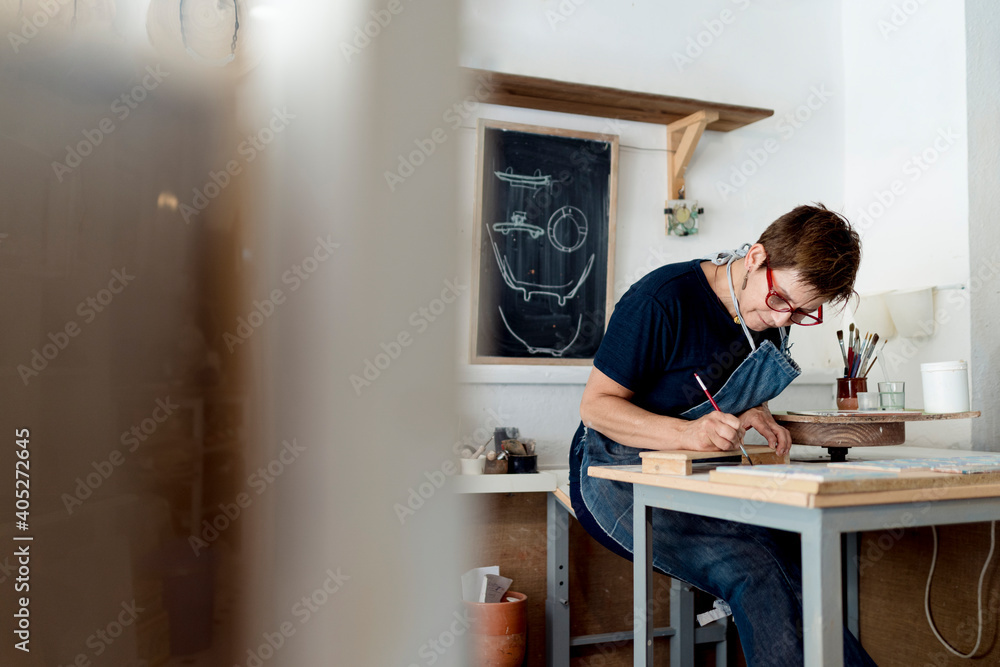 Female creative professional painting while sitting in ceramic workshop Female creative professional painting while sitting in ceramic workshop