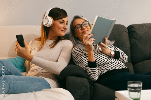 Mother showing book to daughter using mobile phone while sitting on sofa at home photo