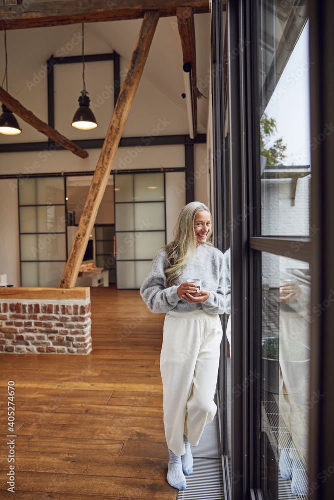 Happy woman with coffee cup leaning on glass door at home Happy woman with coffee cup leaning on glass door at home