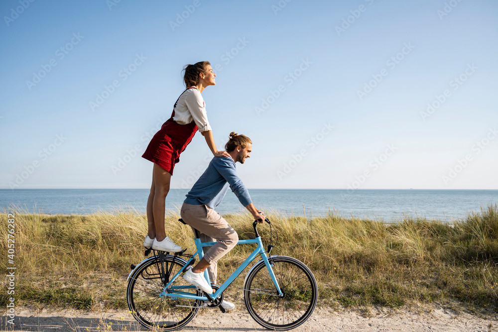 Girlfriend enjoying ride with man while standing on bicycle against clear sky Girlfriend enjoying ride with man while standing on bicycle against clear sky