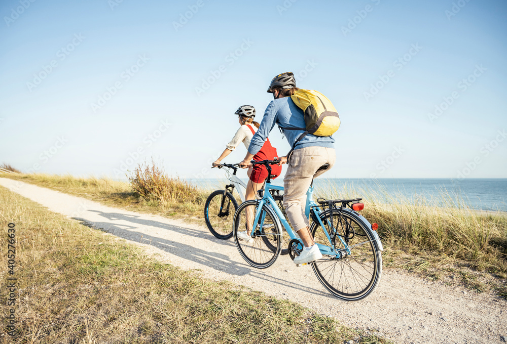 Man with backpack cycling bicycle with woman on footpath during sunny day Man with backpack cycling bicycle with woman on footpath during sunny day