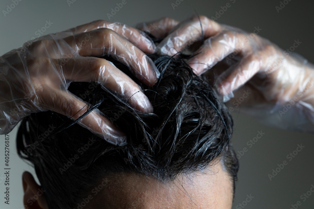 Naklejka premium Closeup woman hands dyeing hair. Middle age woman colouring dark hair with gray roots at home